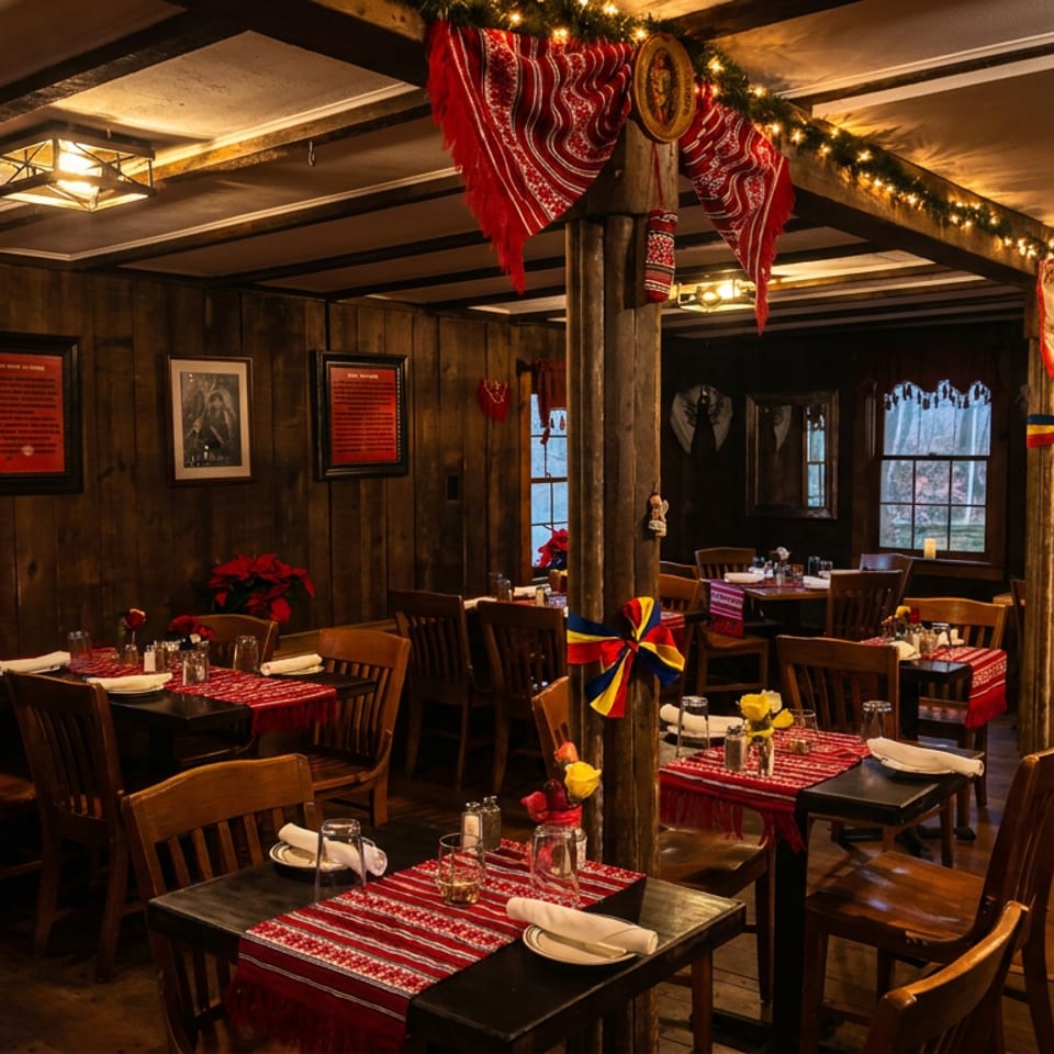 Warmly lit rustic restaurant dining room with wood walls, red patterned table runners, festive decorations, and neatly set tables.